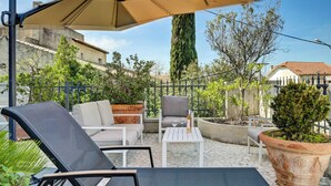 Een terras met tuinmeubilair, waaronder een loungestoel, een bank en een kleine tafel met een glas.