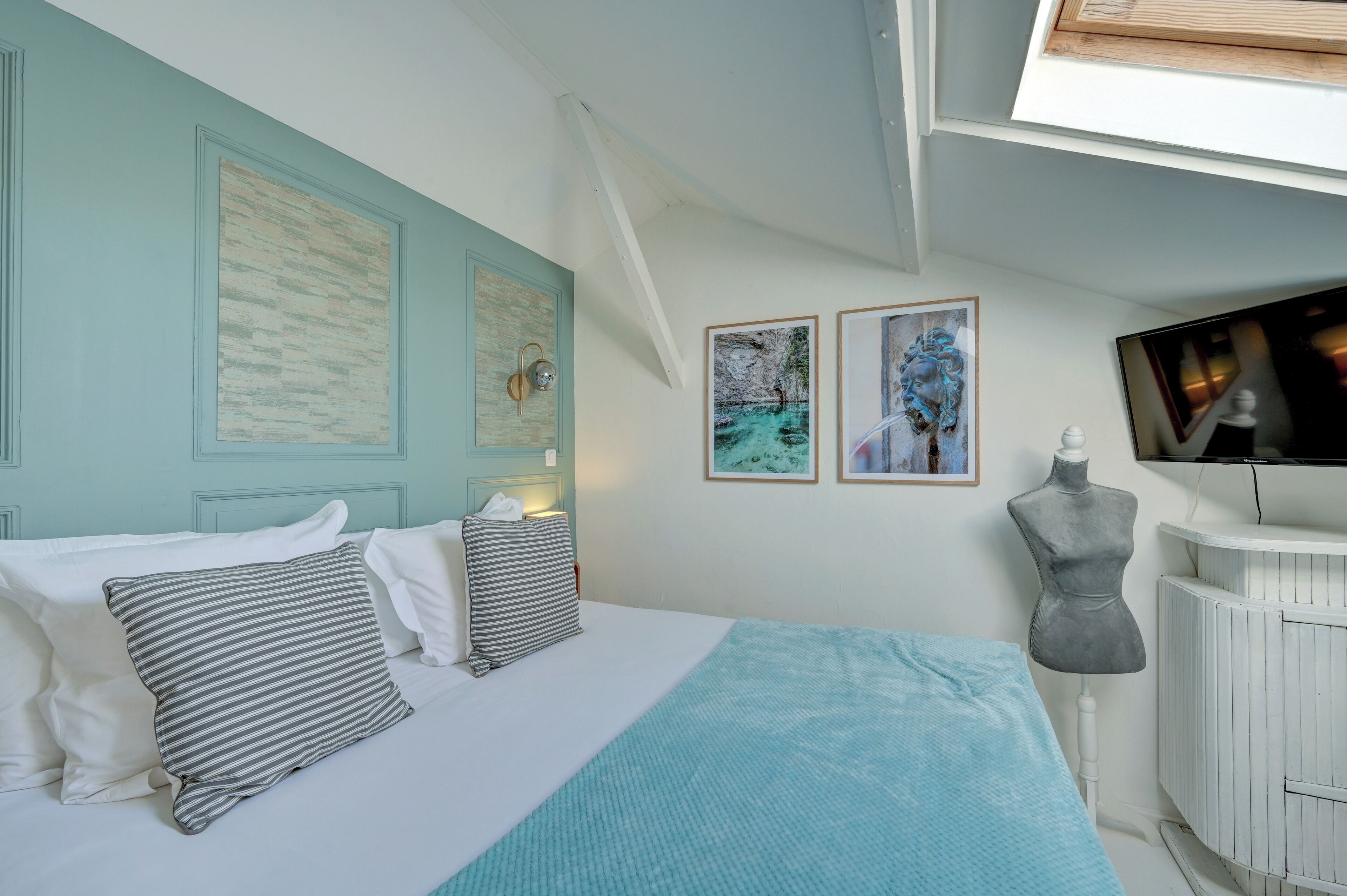 A bedroom with a bed, pillows, a TV, and artwork on the wall.
