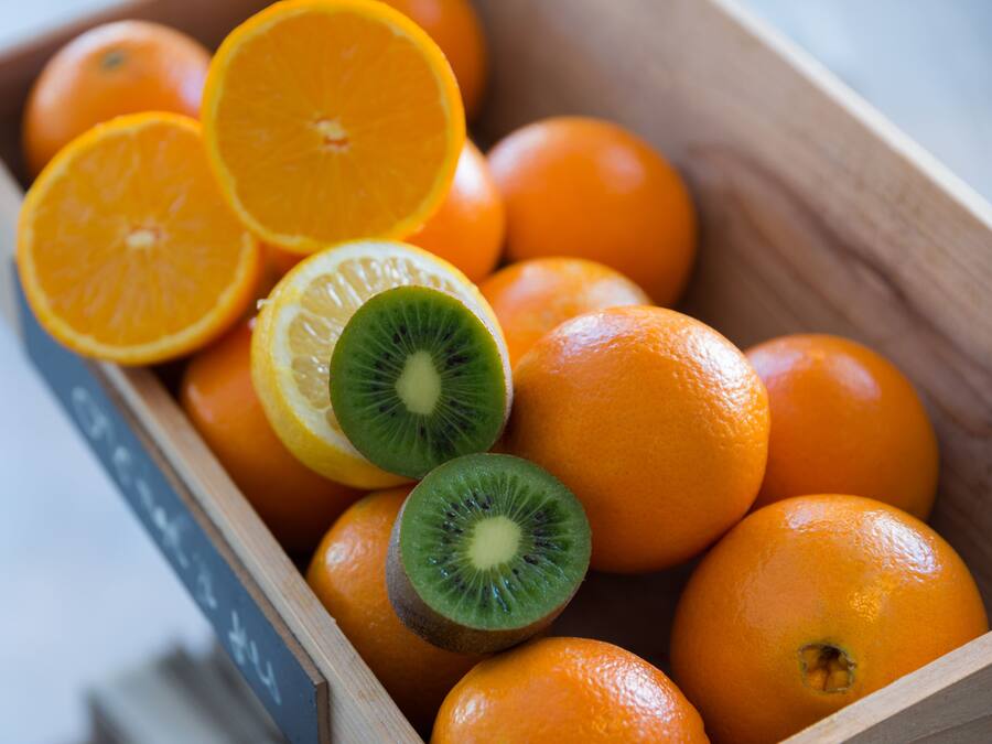 Una caja de madera llena de naranjas y un kiwi cortado.
