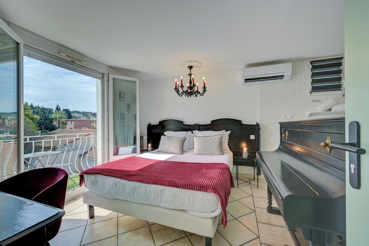 Une chambre à coucher avec un lit, un lustre, un piano et un balcon offrant une vue sur la ville.