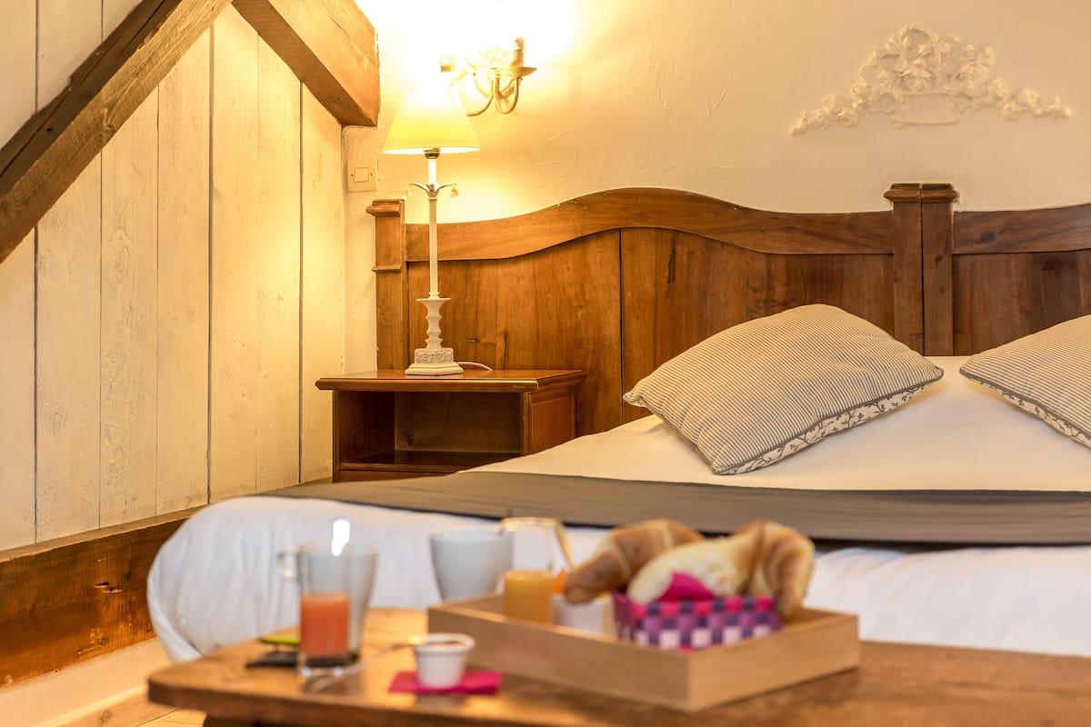 Une chambre d’hôtel confortable, avec une tête de lit en bois, une table de chevet avec une lampe et un plateau contenant des articles pour le petit-déjeuner.