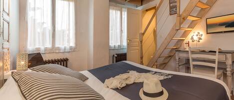 A bedroom with a bed, striped pillows, a hat, and a view of a staircase leading to an upper level.