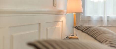 A room with a bedside table, a lamp, and a window with sheer curtains.