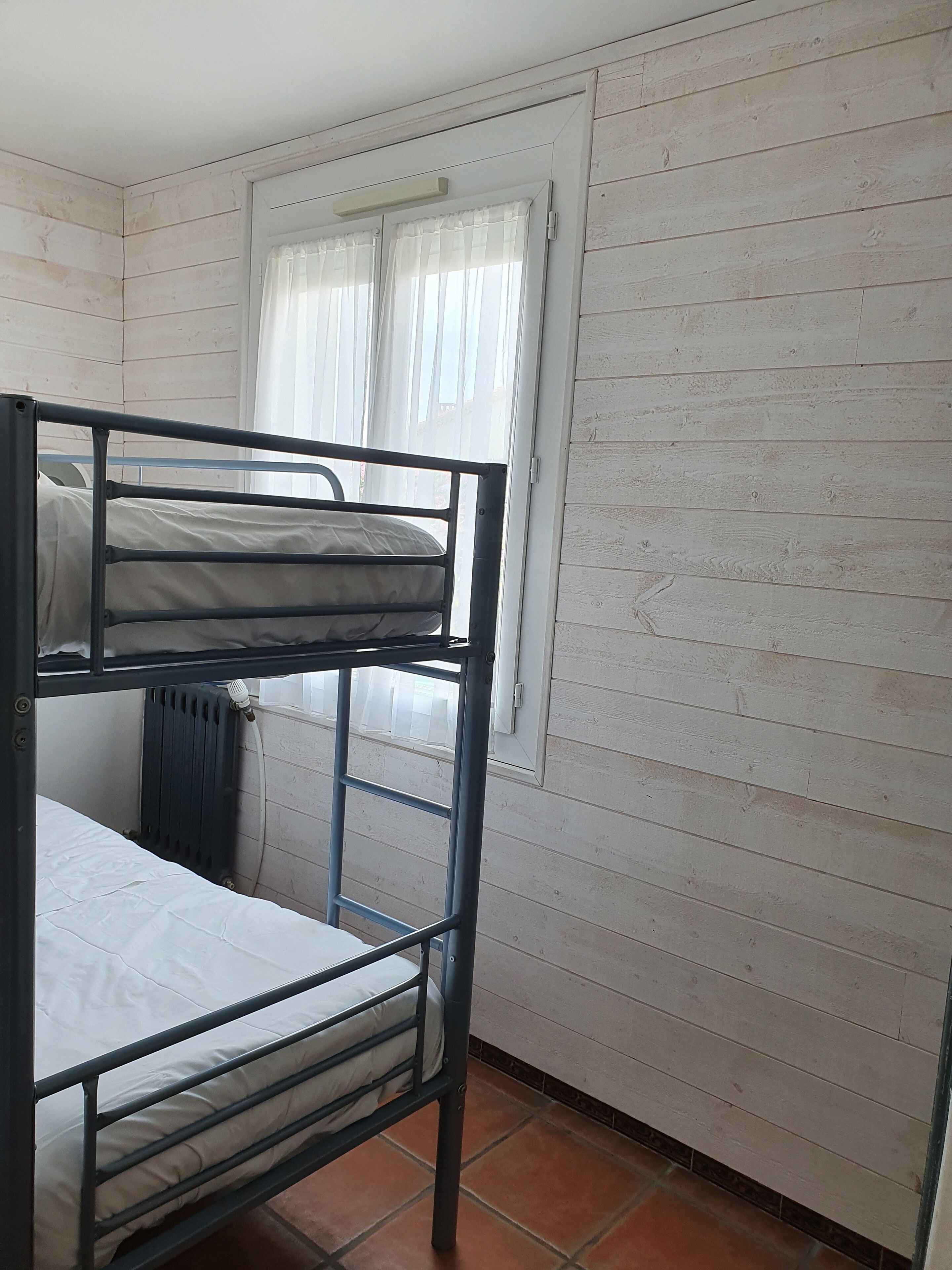 Habitación con literas, paredes blancas y ventana con cortinas traslúcidas.
