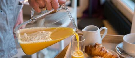 A person pouring orange juice into a glass on a tray with croissants and cups.