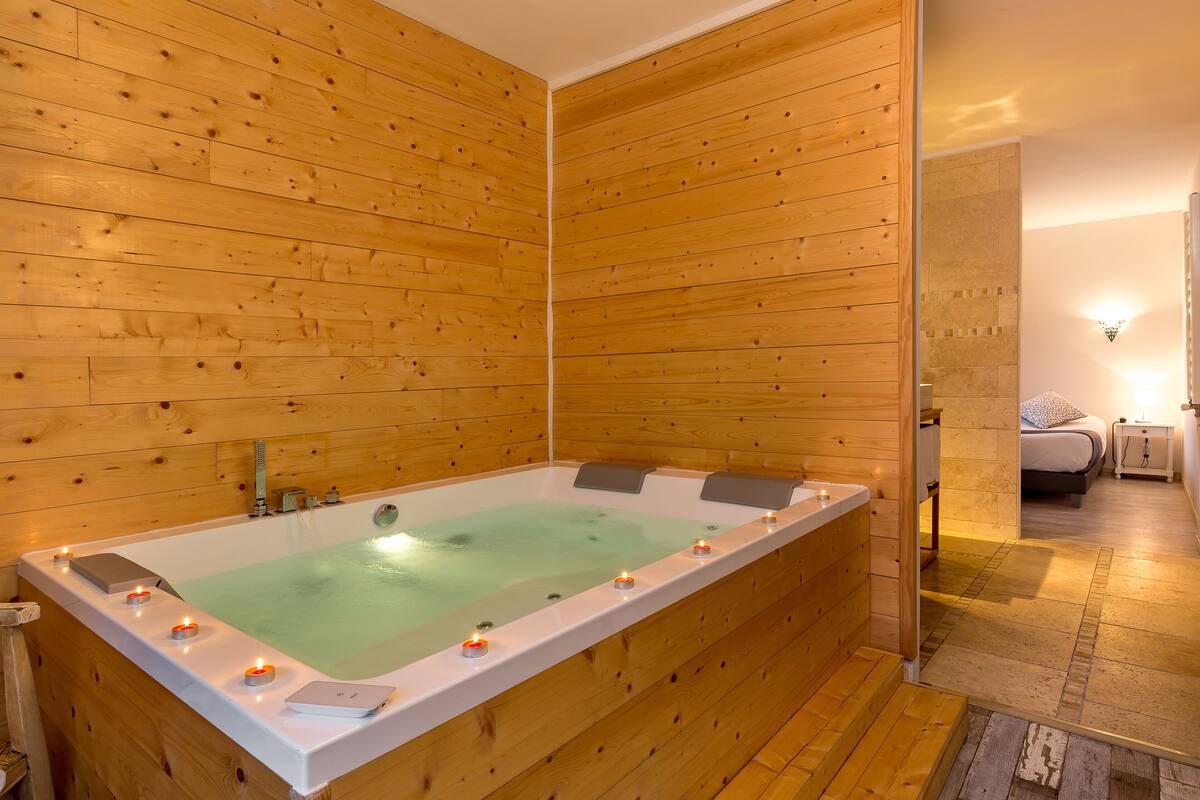 Une pièce aux murs lambrissés, avec une grande baignoire, une petite table de chevet et un lit.