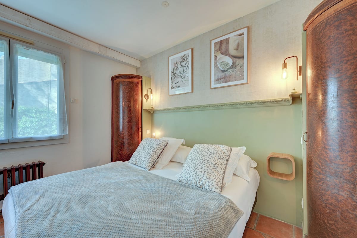 Une chambre à coucher avec un lit, un radiateur, une fenêtre avec des rideaux et des luminaires fixés au mur.