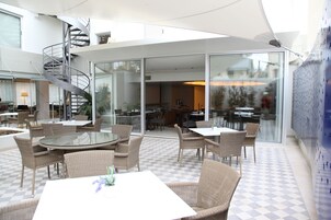 Un comedor moderno y luminoso con muebles de mimbre, puertas de vidrio que dan a un patio exterior y una escalera en espiral.