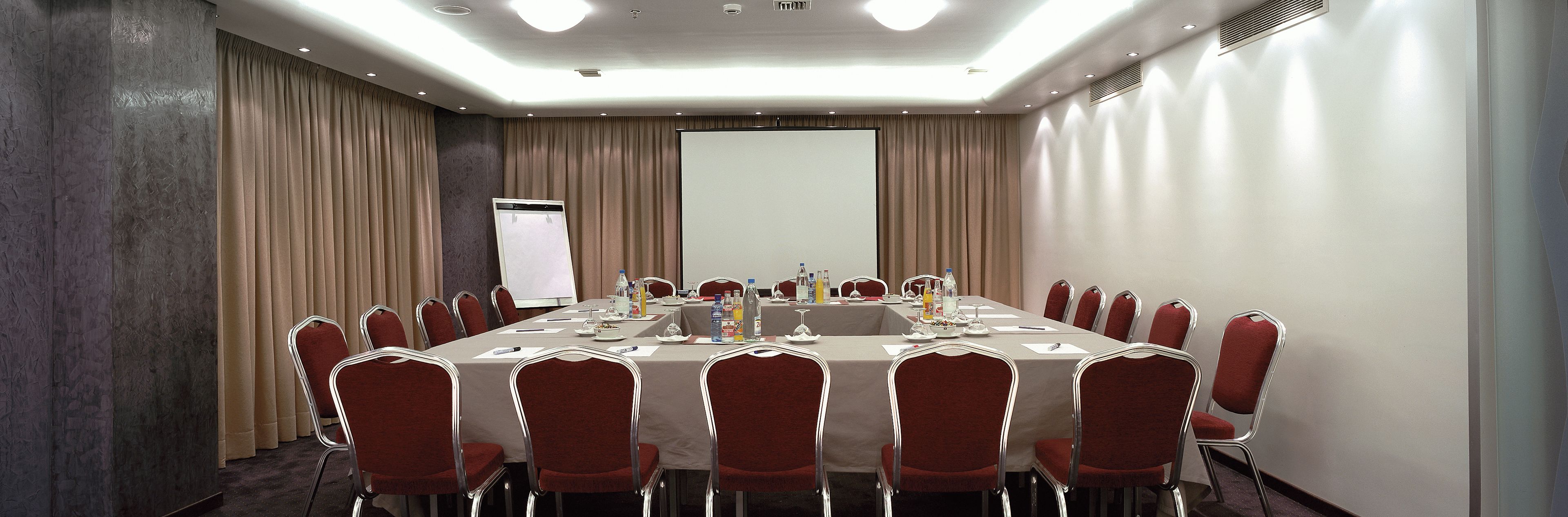 A conference room with a long table, red chairs, and a projector screen.