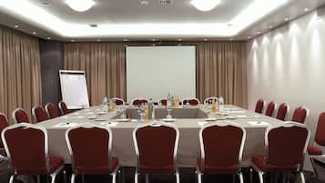 Un salón de conferencias con una larga mesa, sillas rojas y una pantalla de proyector.