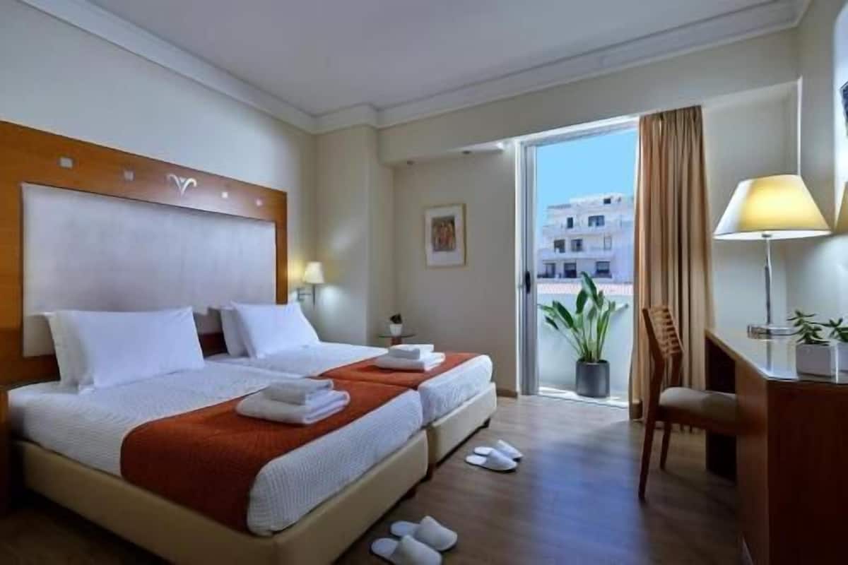 A hotel room with a bed, a desk, a chair, a window with a view, and a balcony.