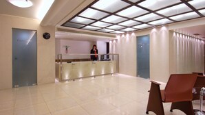 A hotel reception area with a glass partition, a receptionist, and a reception desk. - Atrion Hotel (Heraklion)