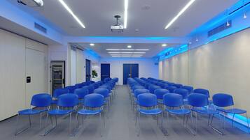 A conference room with rows of blue chairs, a projector, and ceiling lights.