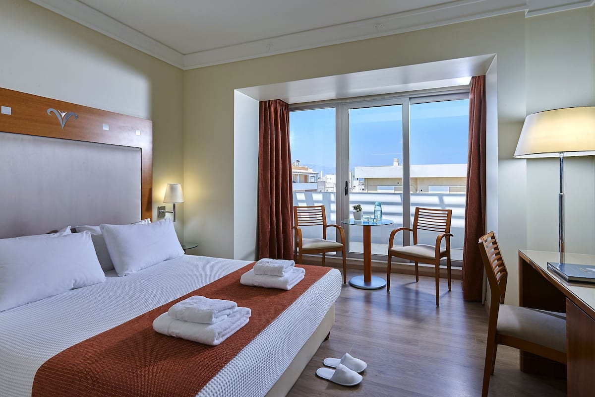 A hotel room with a bed, a desk, a chair, a table, and a view of the sea.