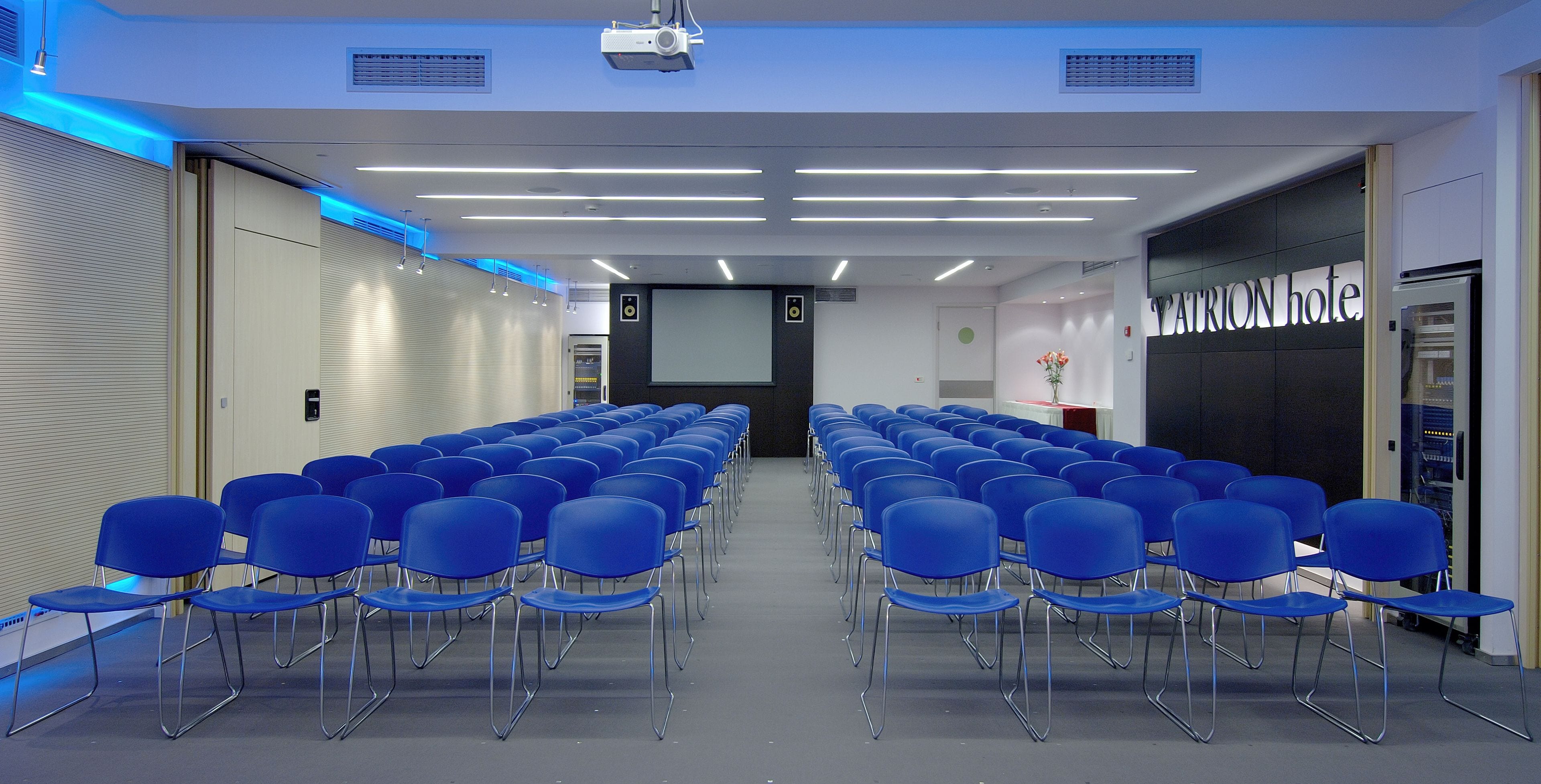 A conference room with rows of blue chairs, a projector screen, and a sign for "ATON hotel".