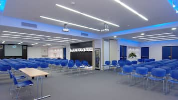 Ett konferensrum med rader av blå stolar, en projektor och en skärm.