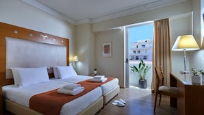 A hotel room with a large bed, a desk, a chair, and a balcony with a view of buildings. - Atrion Hotel (Heraklion)