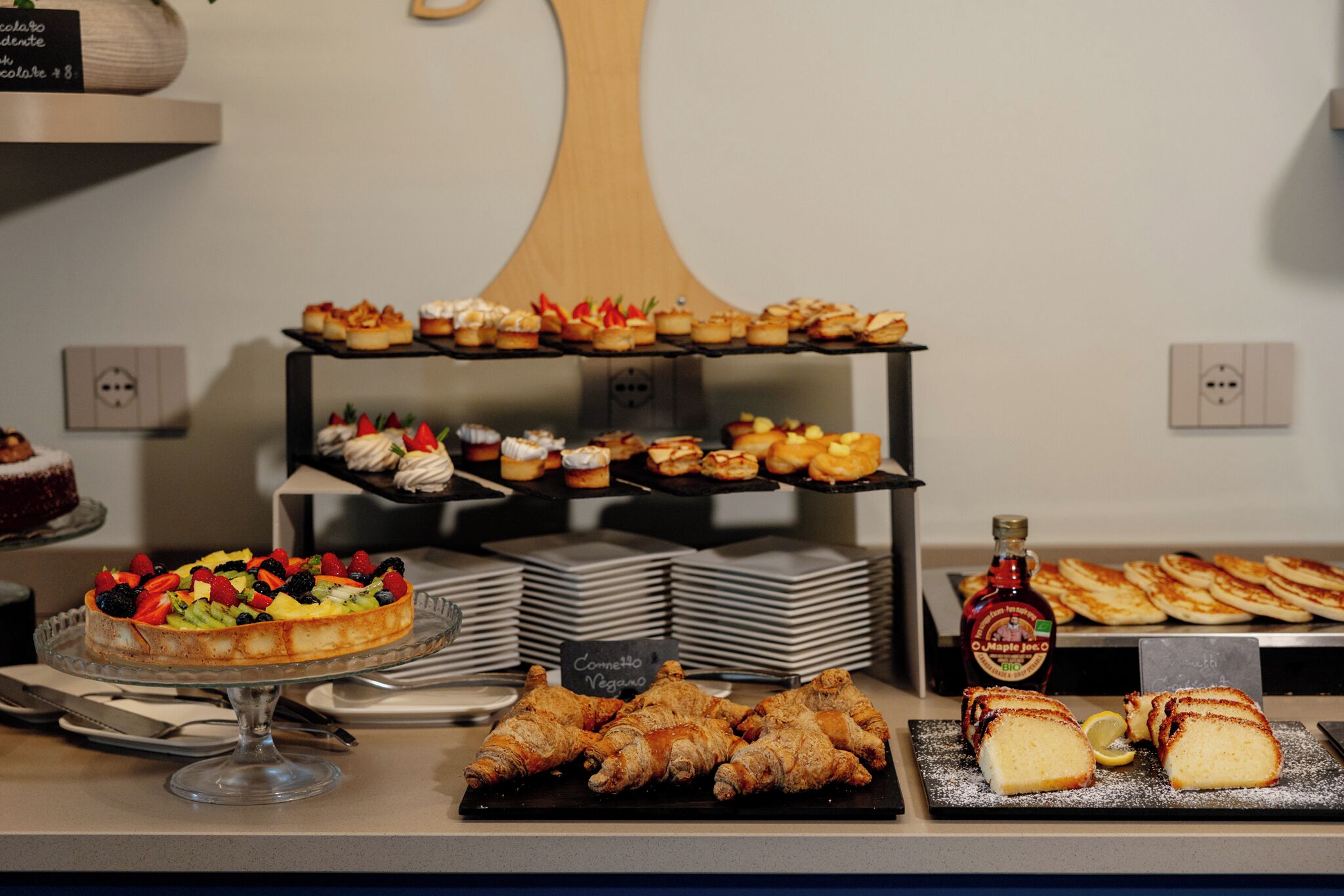 En buffet med forskellige spiser, herunder en frugttærte, bagværk og en flaske ahornsirup.