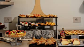 A buffet with various food items including a fruit tart, pastries, and a bottle of maple syrup.