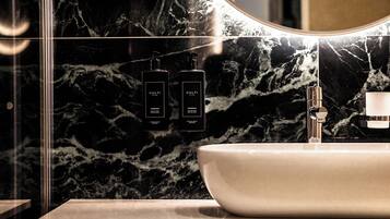 A bathroom with a marble sink, a mirror, and two black bottles labeled 'CULTI' on the wall.