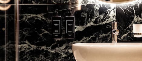 Un baño con lavamanos de mármol, un espejo y dos botellas negras con la etiqueta 'CULTI' en la pared.