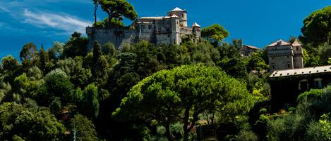 A historic stone castle atop a hill, surrounded by dense greenery and a clear blue sky.