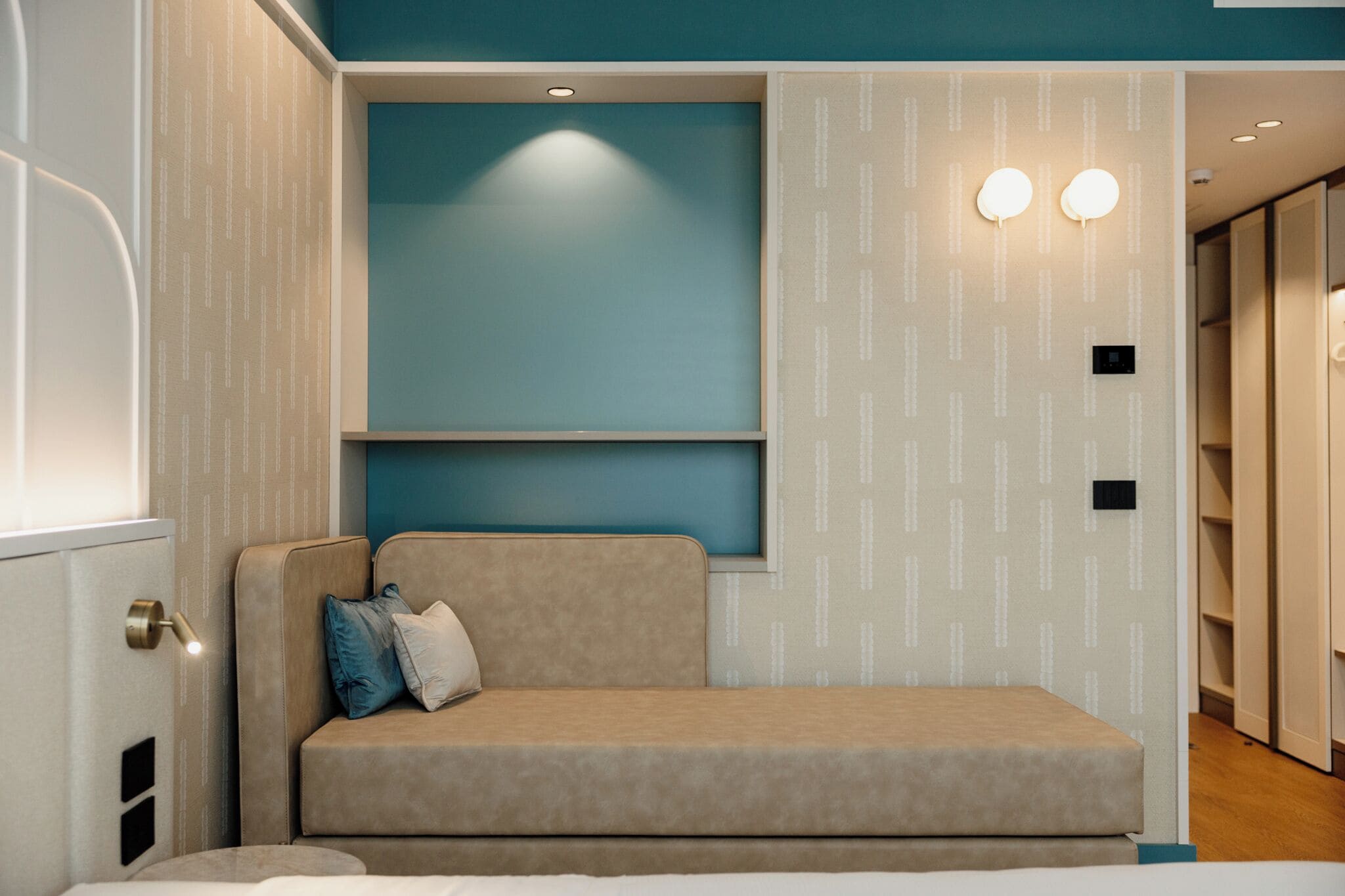 A modern room with a sofa, a wall-mounted light fixture, and a patterned wallpaper.
