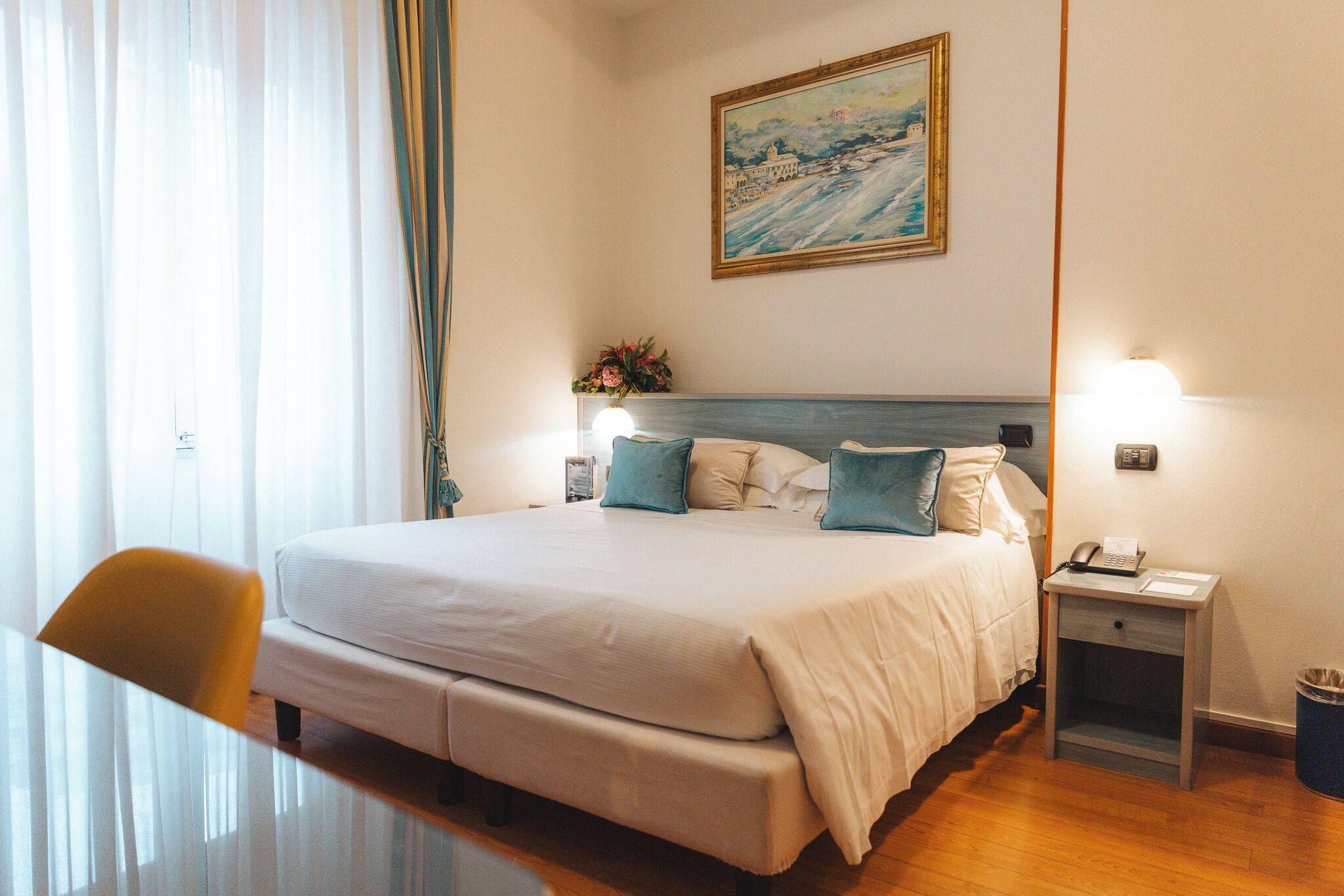 Une chambre d’hôtel avec un grand lit, des tables de chevet, une chaise, un tableau au mur et une fenêtre avec des rideaux.