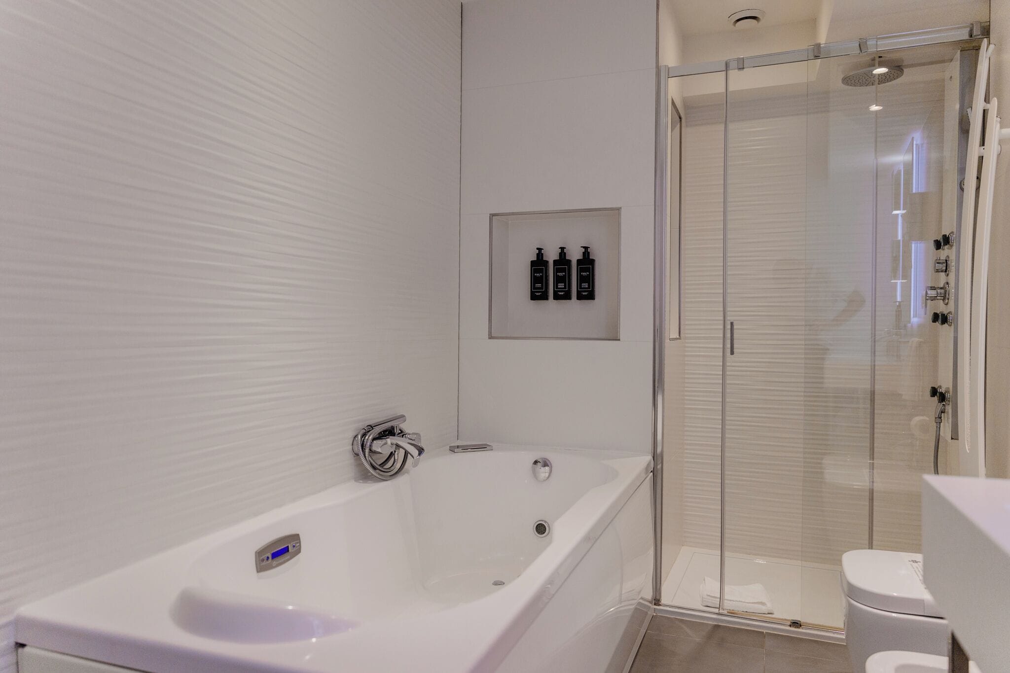 A modern bathroom with a white bathtub, a glass-enclosed shower, and a toilet.