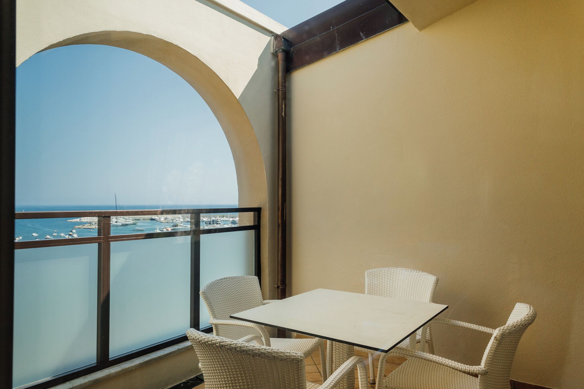 Un balcone con tavolo e sedie, vista su un porto turistico con barche.