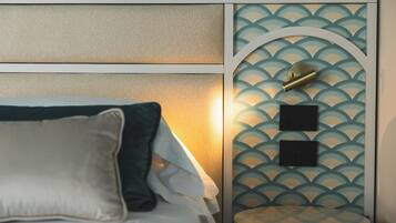 A neatly made bed with pillows, a headboard with a textured panel, and a wall with a decorative pattern and two wall-mounted items.
