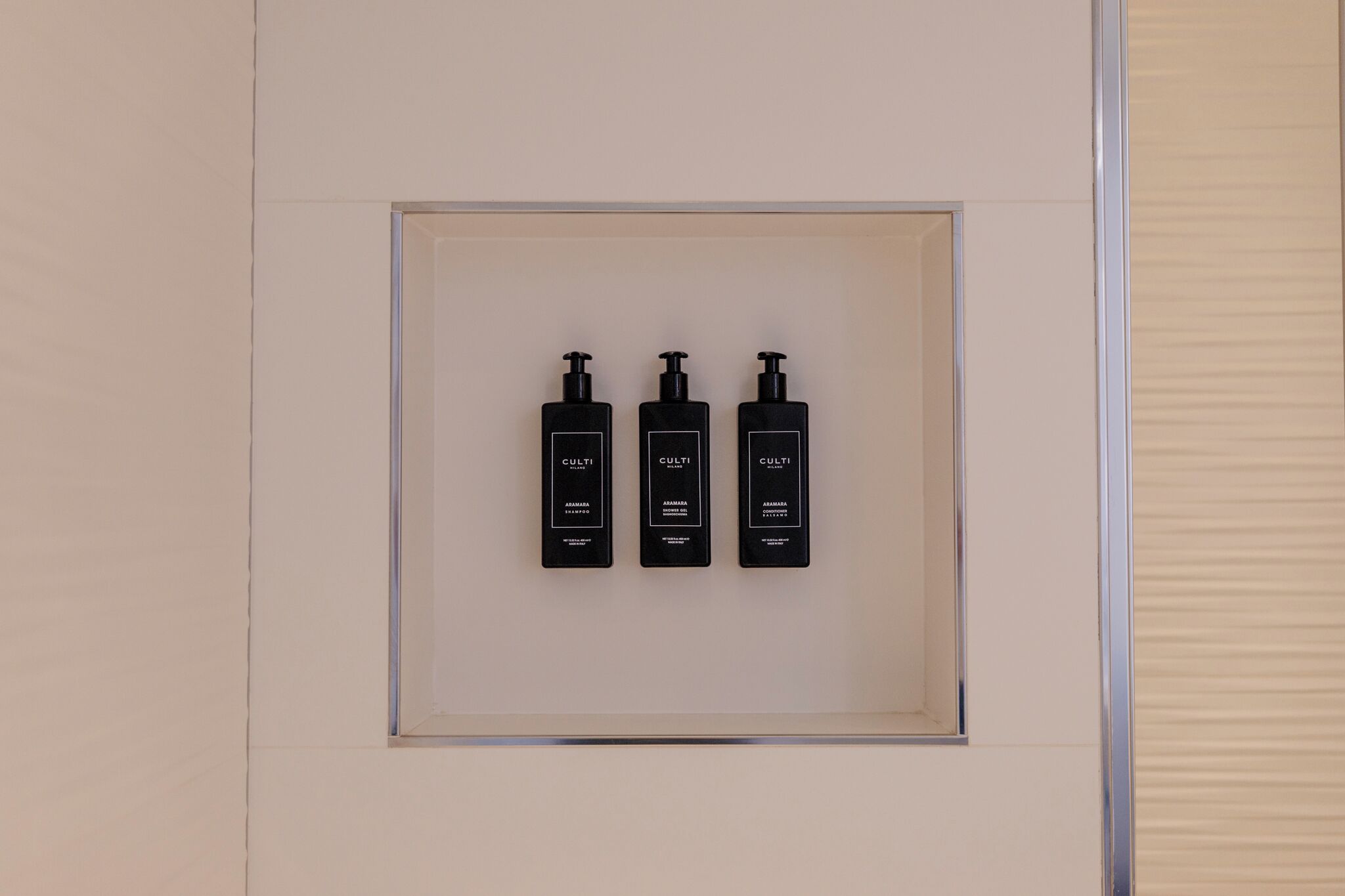 Tre flaconi neri di shampoo, balsamo e bagnoschiuma Culti disposti in un quadro quadrato sulla parete.
