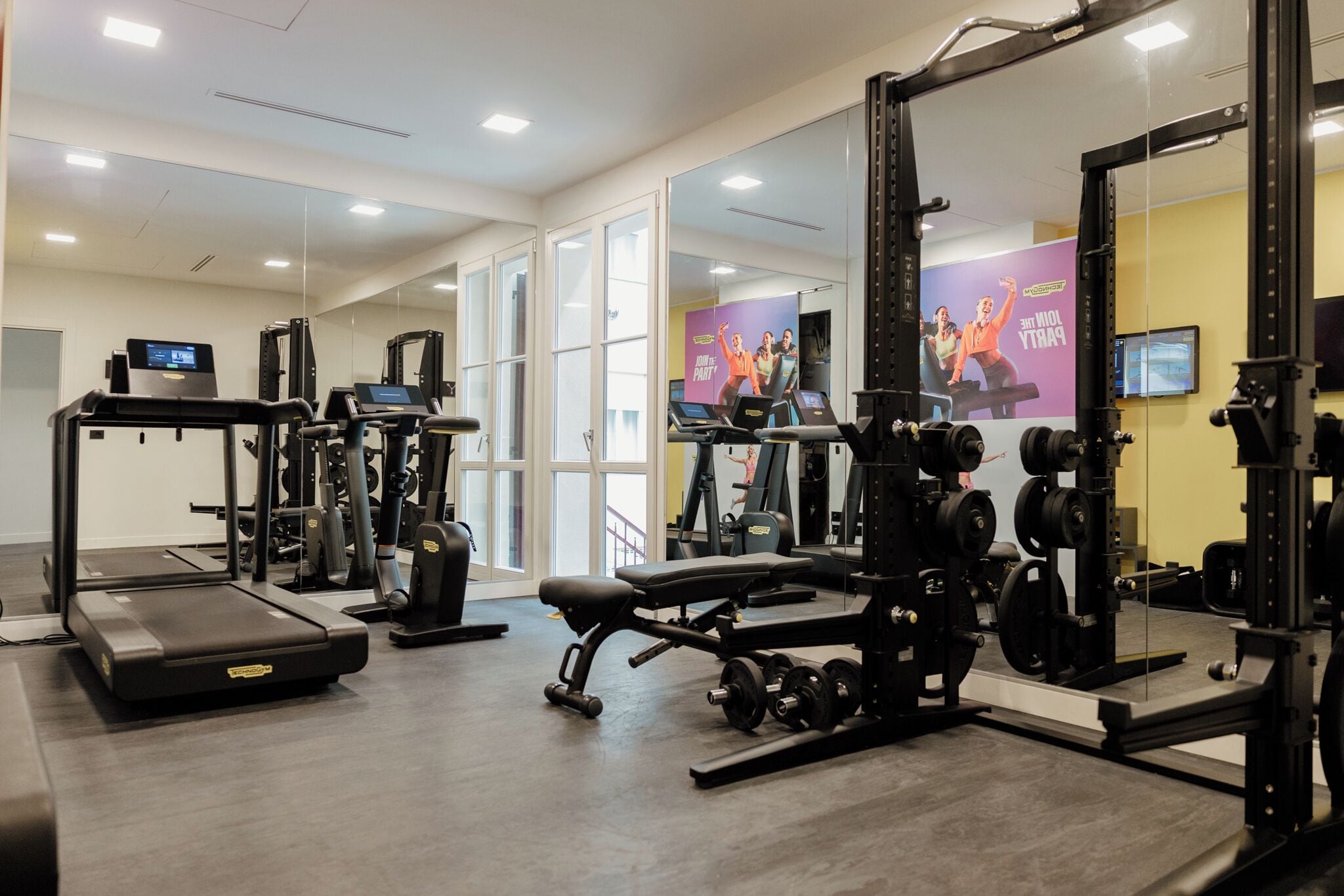 Une salle de sport équipée de machines de cardio, de matériel de musculation et de miroirs.