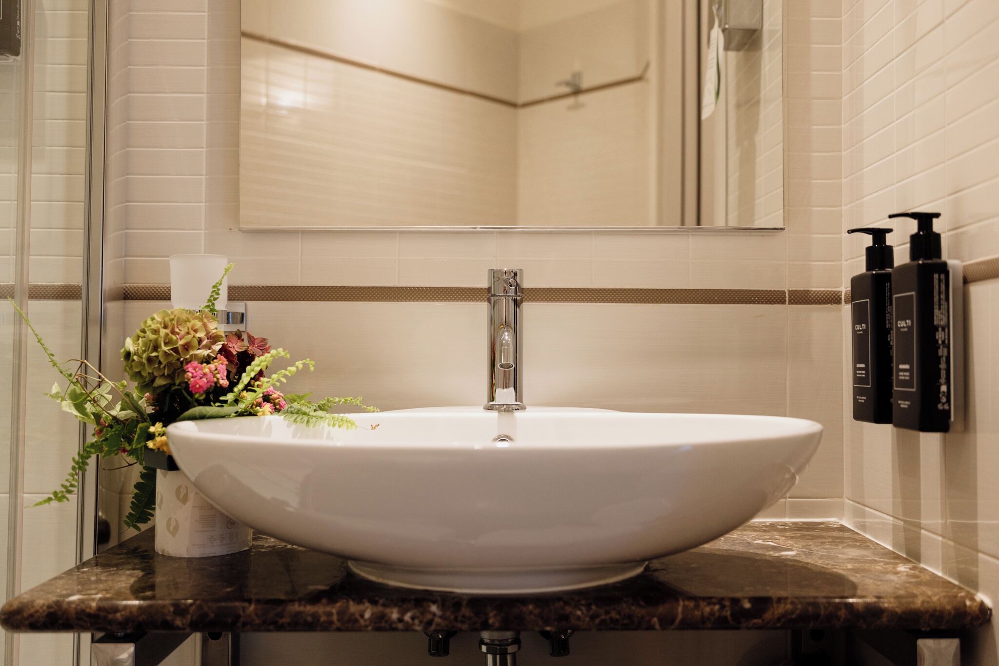 A bathroom with a large white sink, a mirror above it, and a vase of flowers on the counter.