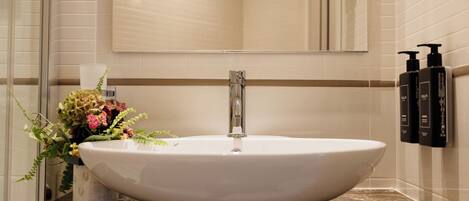 Un baño con un lavamanos blanco grande, un espejo encima y un florero sobre la encimera.