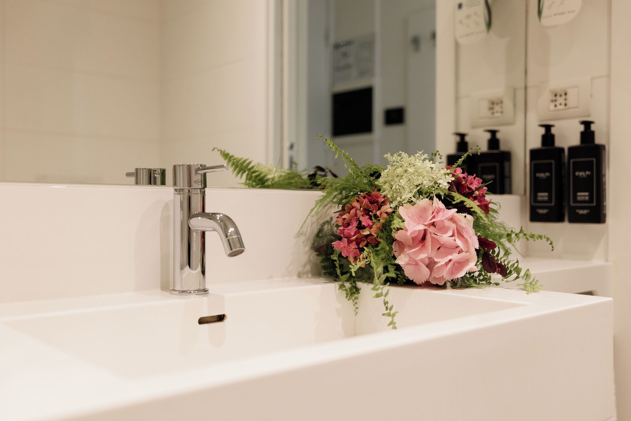 A bathroom with a white sink, a chrome faucet, and a mirror.