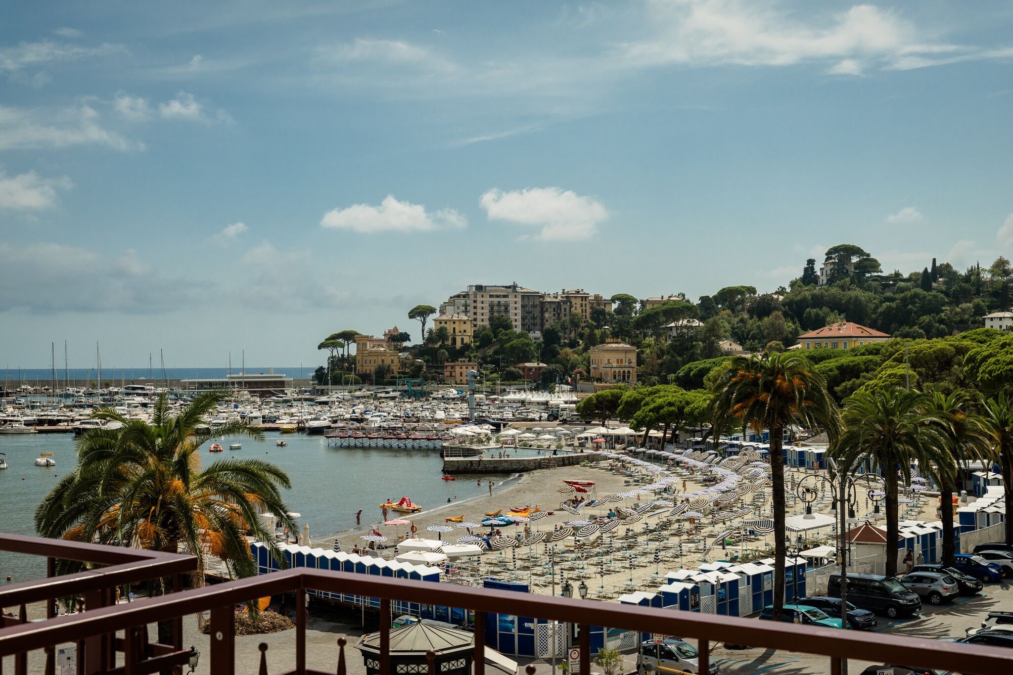 A marina with boats, a beach with umbrellas, and buildings in the background.