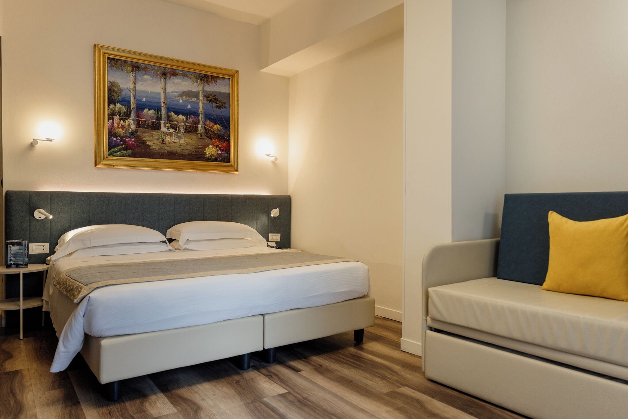 A bedroom with a bed, bedside tables, a painting, a sofa, and a nightstand.