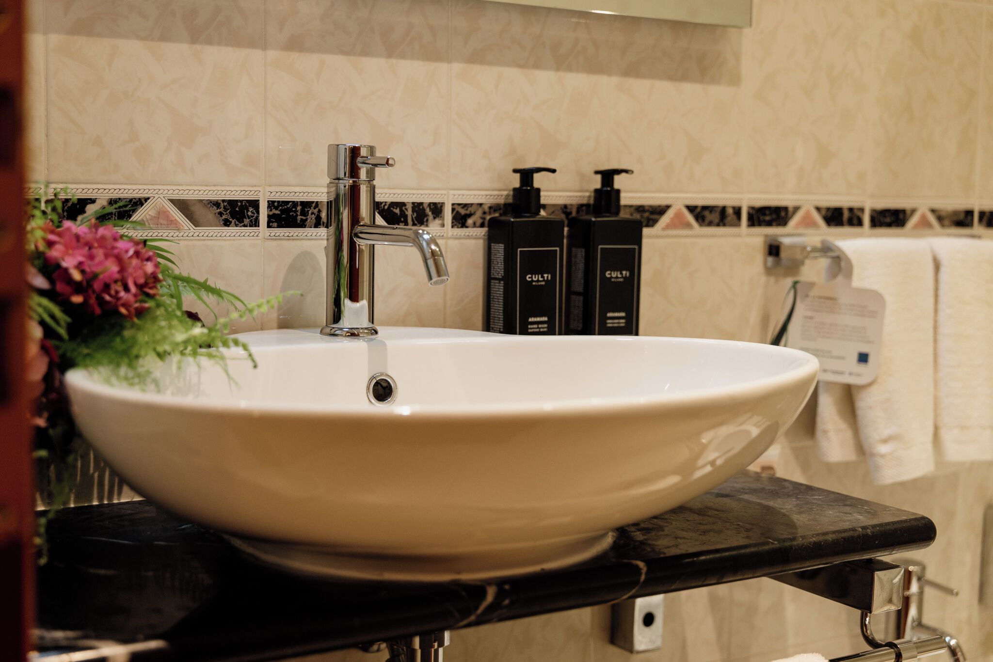 Ein Badezimmer mit einem großen, weißen Waschbecken, einem modernen Wasserhahn und zwei schwarzen Pflegeprodukten an der Wand.