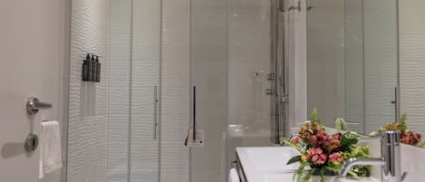 A modern bathroom with a glass-enclosed shower, a white sink with a mirror, and a vase with flowers.