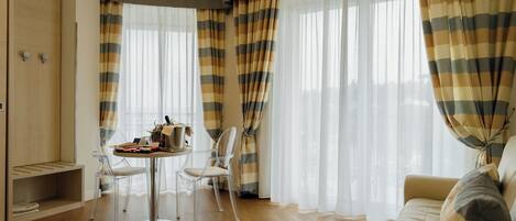 Ein Zimmer mit Holzboden, einem runden Tisch mit Stühlen, einem Sofa und großen Fenstern mit gestreifteren Vorhängen.