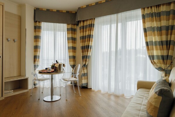 A room with a wooden floor, a round table with chairs, a sofa, and large windows with striped curtains. - Best Western Plus Tigullio Royal Hotel (Rapallo)