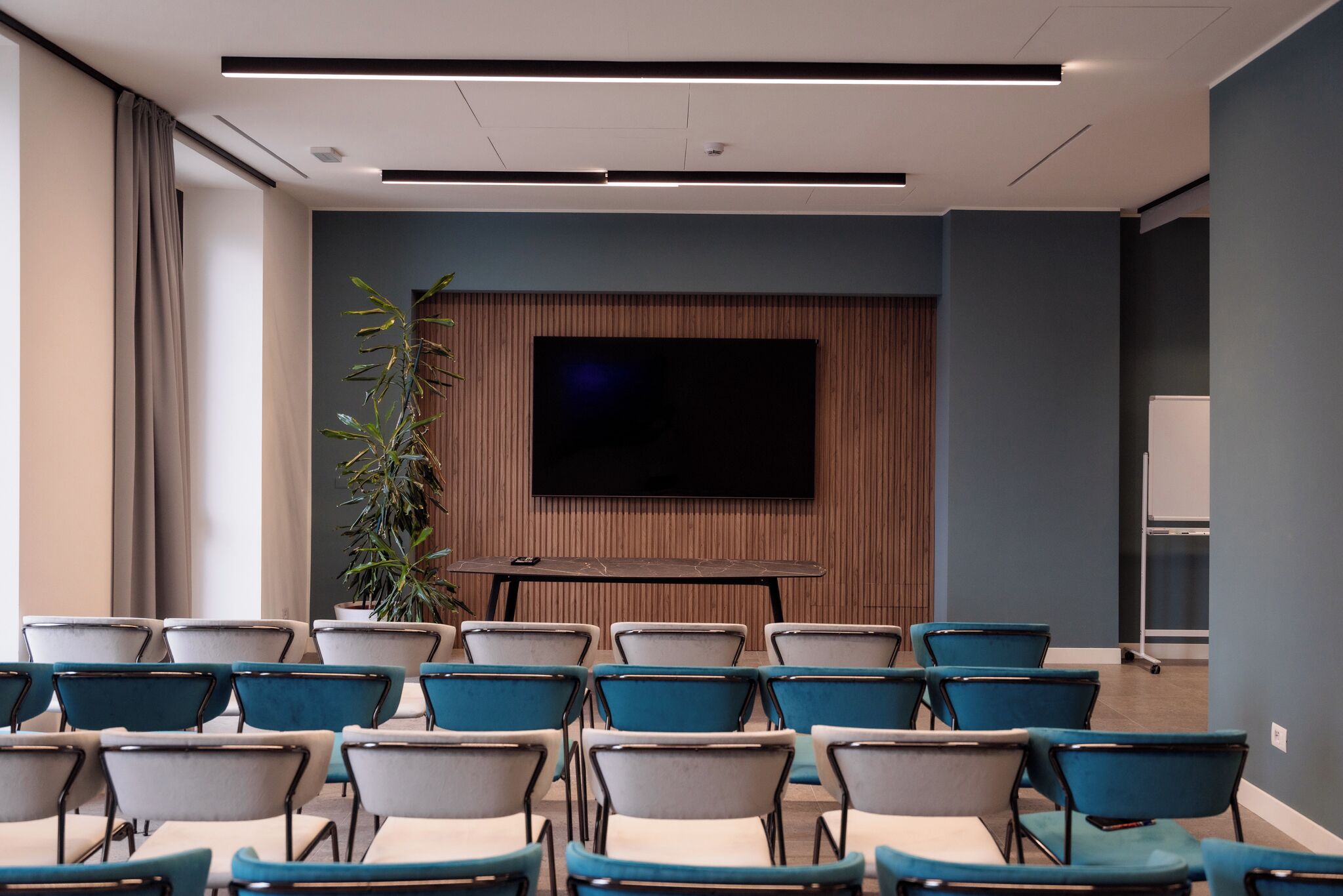 A conference room with rows of chairs, a large flat-screen TV, and a wooden panel wall.