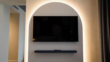 Un interno moderno con una TV a schermo piatto montata su una parete bianca, uno scaffale scuro sotto e un'apertura che dà su un'altra stanza.