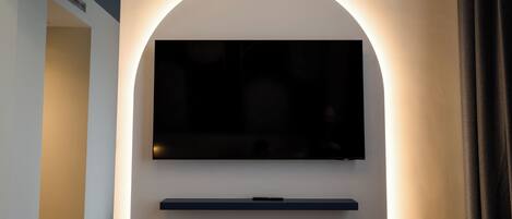 Un intérieur moderne avec un téléviseur à écran plat fixé sur un mur blanc, une étagère sombre en dessous et une porte donnant sur une autre pièce.