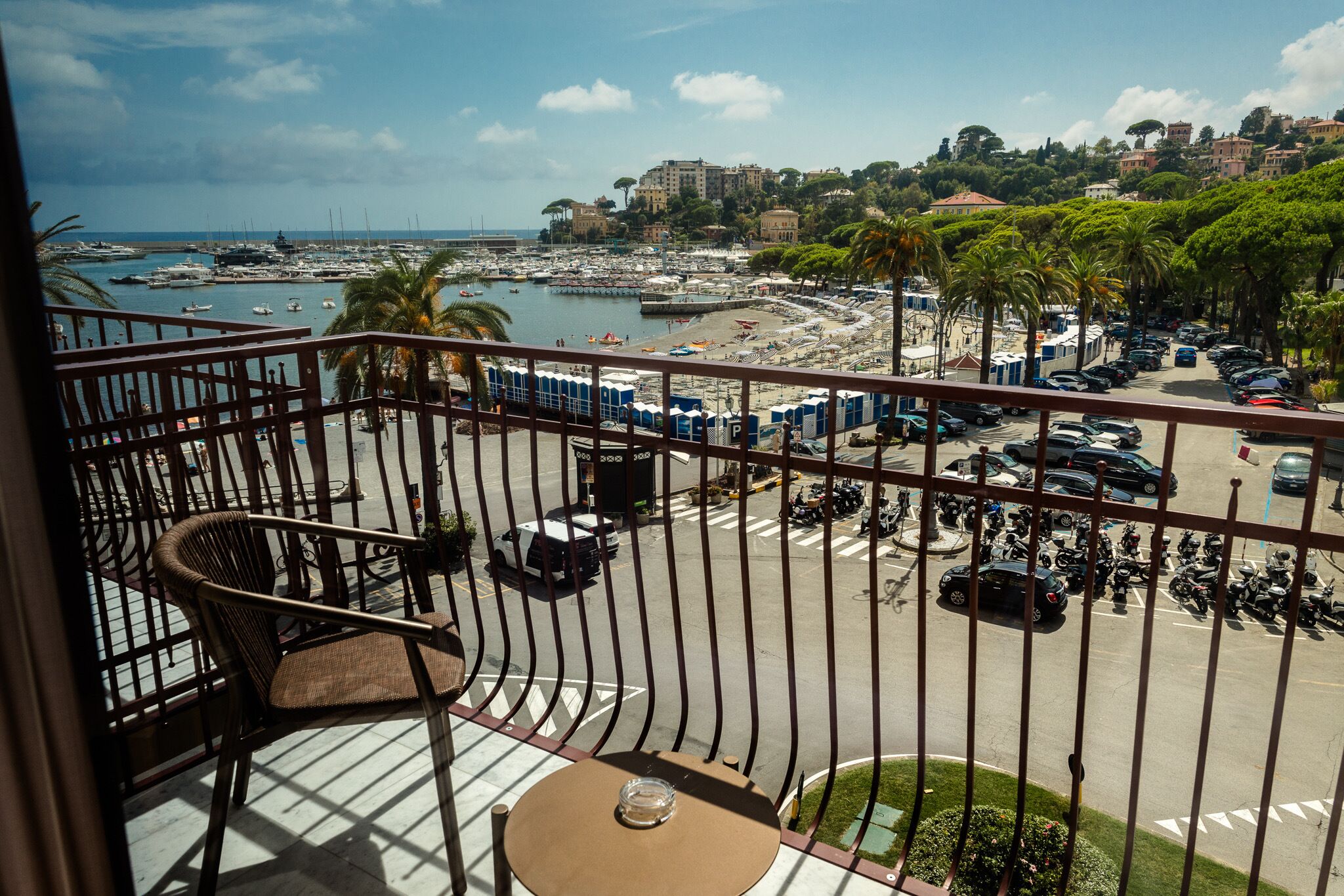 Un balcone con vista su un porto turistico, auto parcheggiate e una collina in lontananza.