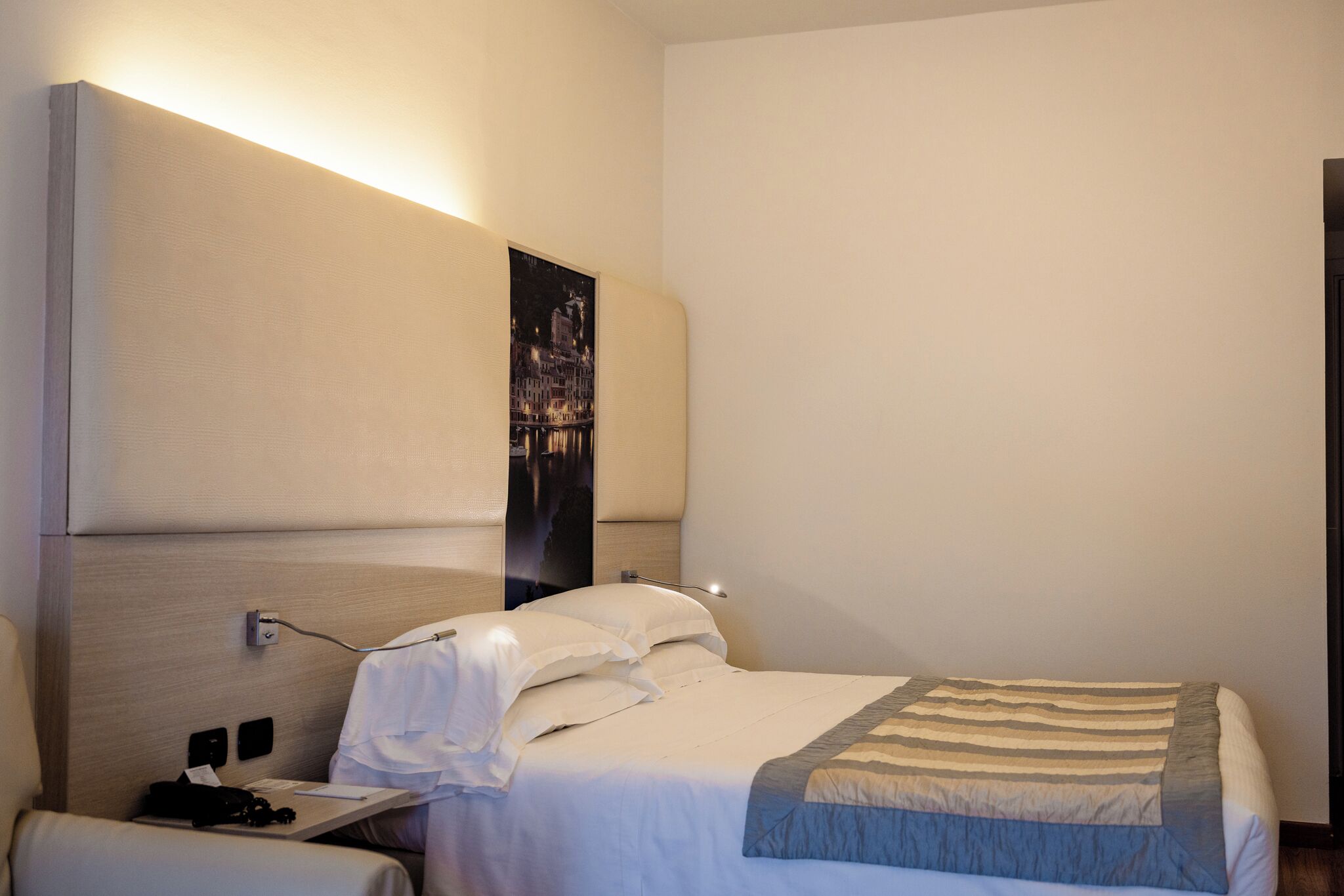 Una camera d'albergo con un letto, un comodino, una lampada e un quadro appeso al muro.