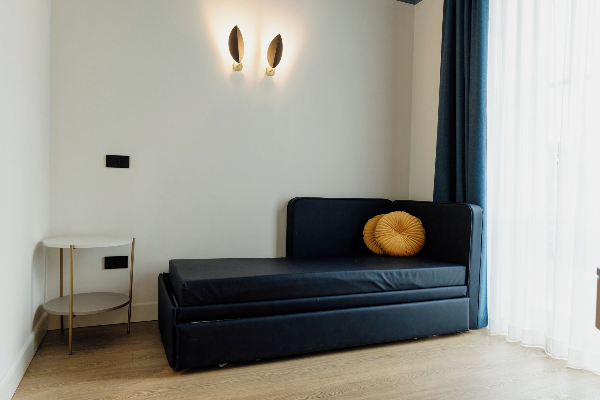 A modern room with a dark blue sofa, a small round table, and a wall-mounted light fixture.