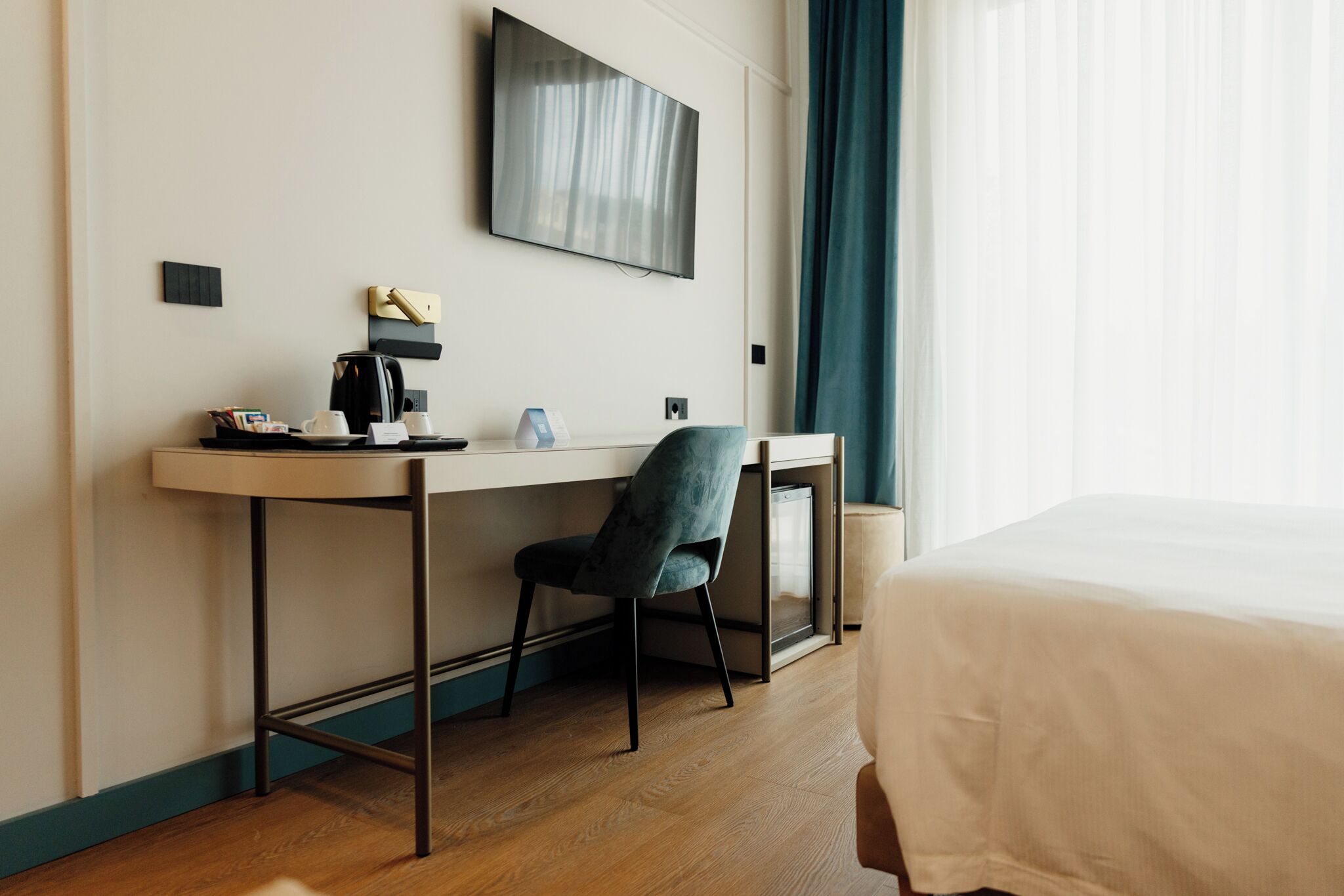 Une chambre d’hôtel équipée d’un lit, d’un bureau, d’une chaise, d’une machine à café et d’un téléviseur fixé au mur.
