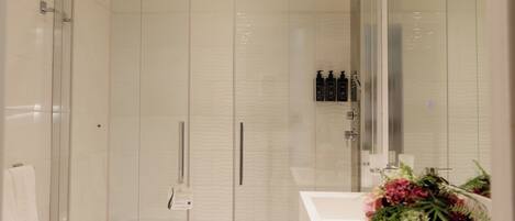 A modern bathroom with a glass shower enclosure, a white sink, and a mirror with a floral arrangement.